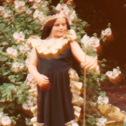 Blurry old photo of a caucasian girl, aged maybe 7, posing in a black and gold flamenco dress, with a crown, black cloth over her head, and holding a stick like a staff
